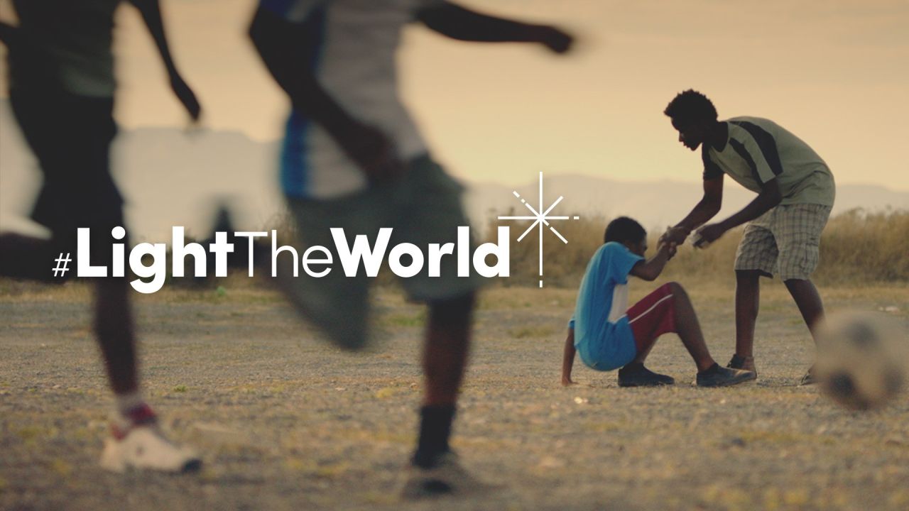 En pojke hjälper en annan pojke resa sig efter att ha ramlat när han spelade fotboll, från videon Ett ljus för världen